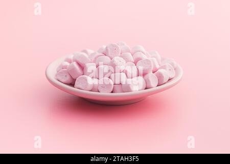 Mini sweet marshmallows candy on plate on the pink background. Stock Photo