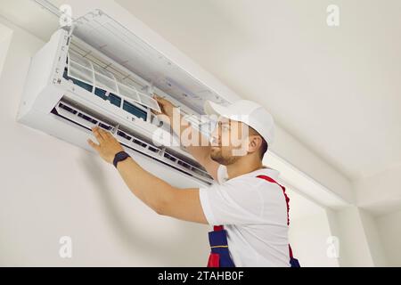 Professional male technician installs indoor air conditioner unit inside office or home. Stock Photo