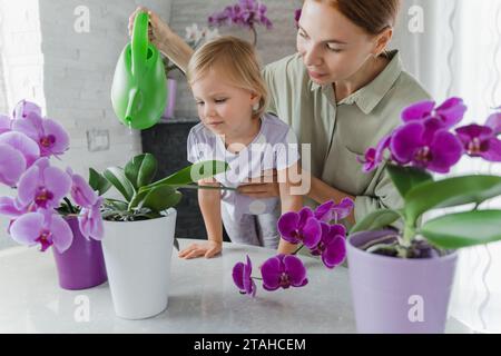 A woman and her little daughter watering orchids from a watering Stock Photo