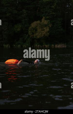 Professional swimmer in a wetsuit swims in open water on a lake. Stock Photo