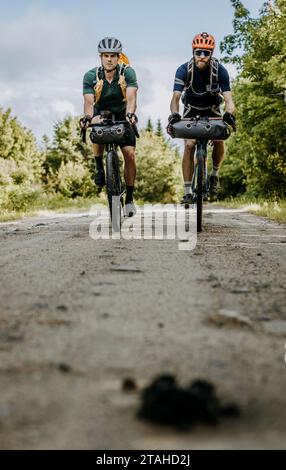 Two men ride heavily laden bikepackign bikes down a dirt road, Maine Stock Photo