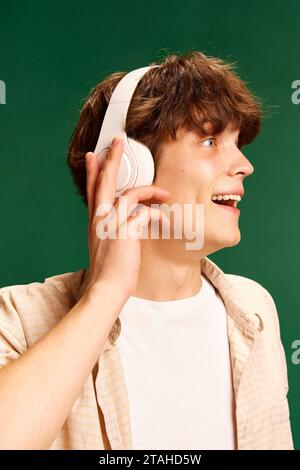 Side view close up portrait of emotional, pleasantly surprised man overjoyed about new song while listening music in headphones against green Stock Photo