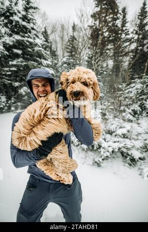 Young man holds his labradoodle dog in snow and cold on walk Stock Photo