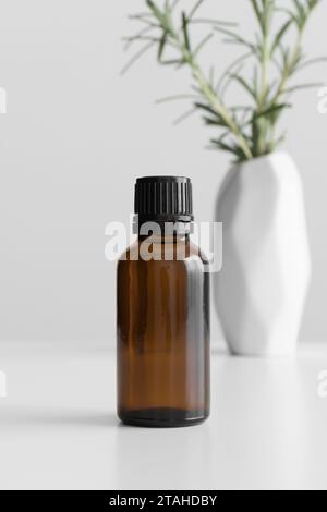 Amber glass essential oil bottle mockup with a rosemary on the white table. Stock Photo