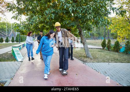 teenage girl teaching skateboarding to boy friend in park Stock Photo