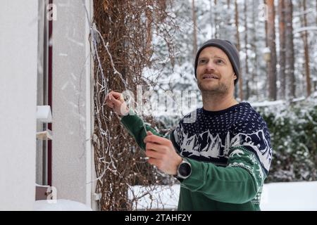 man decorating house exterior with christmas lights on snowy winter day Stock Photo