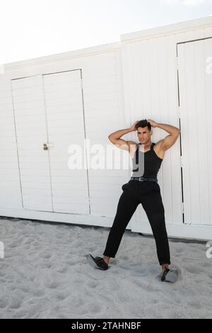 Relaxed and muscular young cuban man in black outfit touching head in Miami, south beach Stock Photo