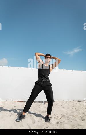 Strong and young cuban man in black outfit touching head and looking at camera in Miami, south beach Stock Photo