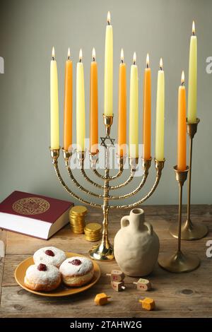 Composition with Hanukkah menorah, dreidels and donuts on wooden table against light background Stock Photo