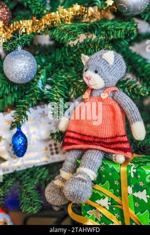 Self knitted kitty sitting on gift boxes under beautifully decorated Christmas tree Stock Photo