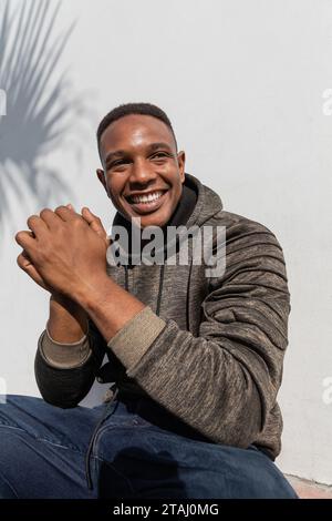 joyful african american man in jeans and hoodie smiling near white wall Stock Photo