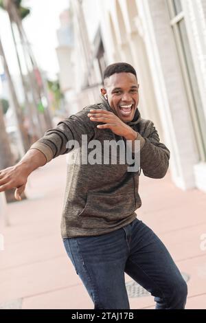 excited african american man in wireless earphone listening music and dancing on street in Miami Stock Photo