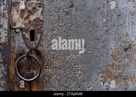 Detail of an aged, worn and weathered wooden doorway with keyhole, knocker ring, cracked wood and a rough texture. Stock Photo
