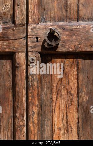 A small, round, metal knocker is mounted to an old, wooden Italian door in Tuscany, Italy. Stock Photo