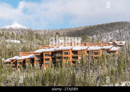 Ski condos covered in snow on the side of a mountain surrounded by snow covered pine trees. Stock Photo