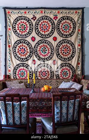 Suzani wall hanging with rug used as tablecloth on dining table in Georgian barn conversion, Tetbury, Gloucestershire, UK. Stock Photo