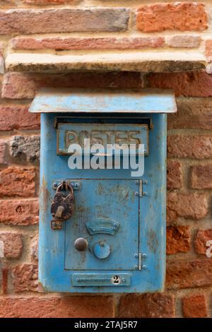 An antique, weathered, blue, metal letter box on a red brick wall with the words Postes, meaning letters and in French, below, "Number of pick ups per Stock Photo