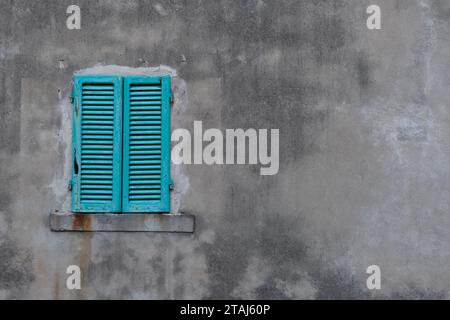 Brightly colored, turquoise, wooden shutters closed in on a large, gray cement wall on a building in Tuscany, Italy. Stock Photo
