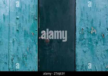 A weathered, wooden, Italian door with turquoise and dark blue-green peeling paint with lock and keyhole. Stock Photo