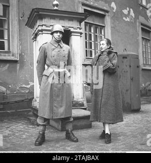 Soldier in the 1950s. A young woman in a warm coat stands admiring a soldier standing guard in front of a guardhouse outside Stockholm Palace. Sweden 1952 Kristoffersson ref BH90-11 Stock Photo