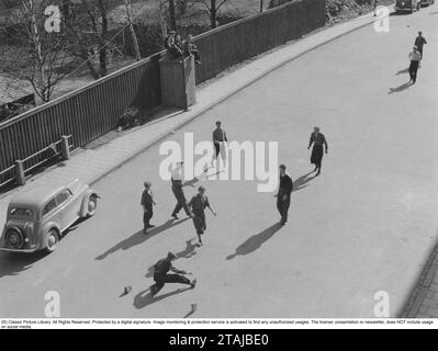 Football in the street. A group of boys play football in the street on a summer day. They have laid two paving stones to mark where the soccer goal is. A harmless pleasure for the youngsters. If a car came, the game stopped, and when the car had passed, it continued. Stock Photo