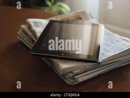 sunlight reflections on digital tablet screen and stack of newspapers on table Stock Photo