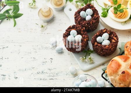 Easter brunch or breakfast. Easter chocolate nest cake with chocolate candy eggs, traditional hot cross buns and deviled eggs with bouquets of bloomin Stock Photo