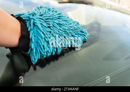 Car wash and self-service concept. A man washes the car windshield with a large blue washcloth. Stock Photo