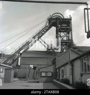 1970s, historical, shaft mining, picture shows a headframe or winding tower - also known as a a pit head- a recognisable feature of a traditionally-built mine shaft - and associated buildings, Sheffield, England, UK. Seen on the top of the shaft structure, the headframe, is the head sheave with hoist. A notice board on a lower level building has a poster saying First Aid Competitions, April 1973 Stock Photo