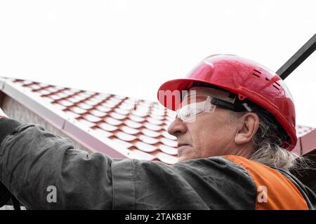 A worker in a helmet and safety glasses works at height. Installation and construction. Stock Photo