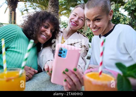 Three middle aged multiracial women pose smiling funny for selfie with mobile. Happy group of mature Stock Photo