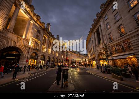 London, UK - Nov 20 2023: Regent Street in central London with Christmas lights overhead. People stand in the middle of the road taking photographs. Stock Photo