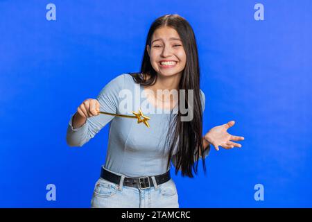 Magician witch young woman gesturing with magic wand fairy stick, making wish come true, casting magician spell, advertising holidays sale discount. Smiling girl isolated on blue studio background Stock Photo