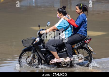 SAMUT PRAKAN, THAILAND, NOV 18 2023, A couple rides a motorcycle through a flooded street Stock Photo