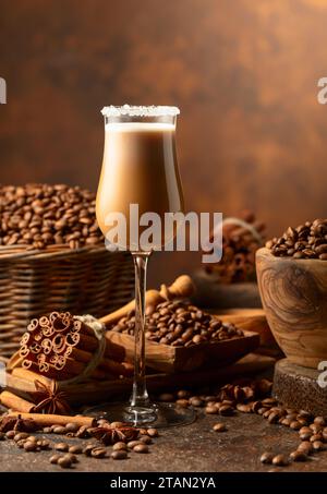 Irish cream and coffee liqueur on a brown background. Coffee beans, cinnamon sticks, and anise are scattered on the table. Stock Photo