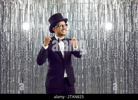 Happy young black guy in glasses, suit and top hat pointing fingers at camera and smiling Stock Photo