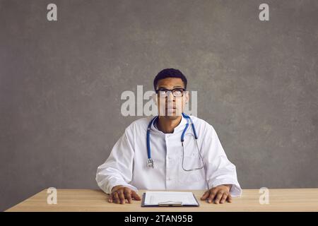 Young black doctor sitting at office desk, looking up and thinking about something Stock Photo