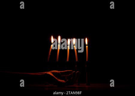 A woman s hand lies on the floor next to shell casings in which there are burning candles in the dark, pain and loss of people, war in Ukraine Stock Photo