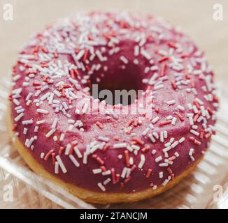 Close-up of a tempting pink doughnut topped with rainbow sprinkles, a delightful treat for dessert or a snack, isolated on a white background. Stock Photo