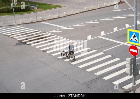 Man crosses the road at a pedestrian crossing and carries a bicycle next to him. View from above. Concept of healthy lifestyle and riding bicycling on Stock Photo