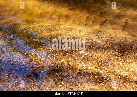 small pebbles in the sand visible through the brown colored river water Stock Photo