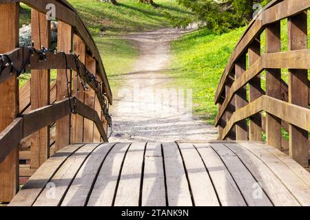 arched boardwalk of wooden planks with a path behind it leading to the forest Stock Photo