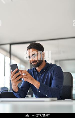 Professional Indian businessman office worker using cellphone at work. Vertical Stock Photo