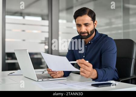 Busy Indian business man reading financial paper checking report in office. Stock Photo