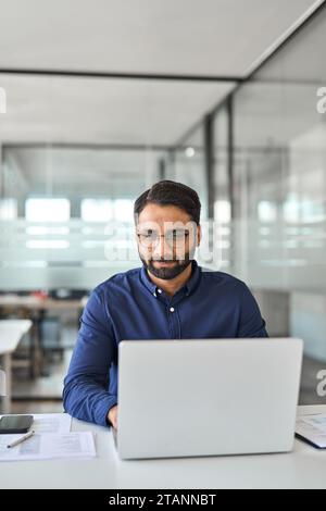 Busy Indian company employee worker using laptop working in office. Vertical Stock Photo