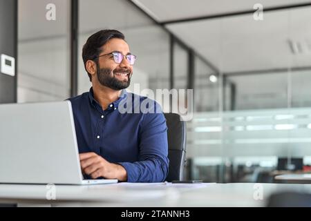 Happy Indian business man ceo executive looking away working on laptop. Stock Photo