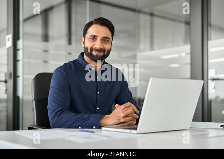 Smiling confident Indian business man sitting at work desk with laptop. Portrait Stock Photo