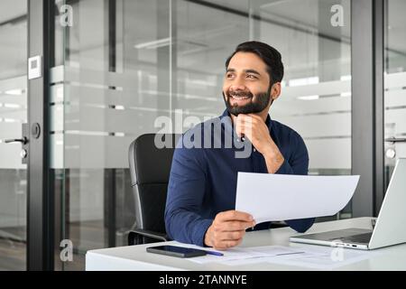 Happy Indian businessman looking away holding report satisfied with work result. Stock Photo