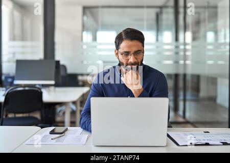 Busy Indian business man thinking on data management working on laptop. Stock Photo