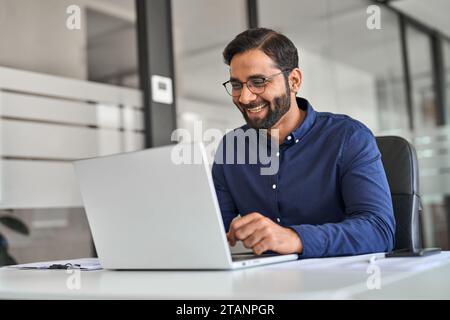 Professional Indian worker looking at laptop feeling happy with work result. Stock Photo